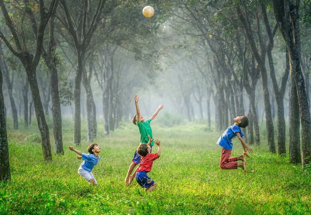 Kinder spielen Ball auf grüner Wiese